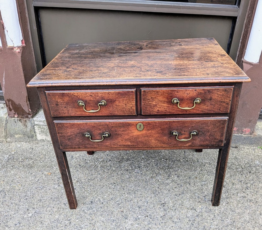 An eighteenth-century dark oak lowboy side table featuring two upper drawers, one long lower drawer, and brass swan-neck handles.