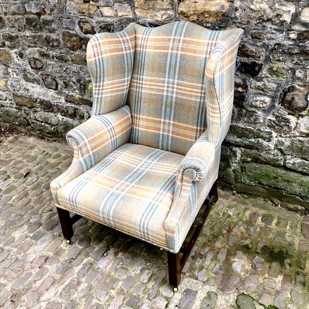 A George III mahogany wing armchair upholstered in a blue, ochre, and cream tartan wool fabric with out-scrolled arms and square legs on brass castors. View II