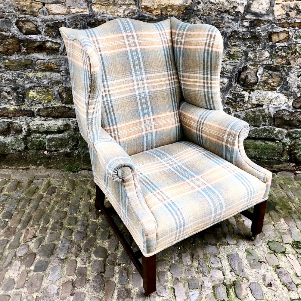 A George III mahogany wing armchair upholstered in a blue, ochre, and cream tartan wool fabric with out-scrolled arms and square legs on brass castors. View III