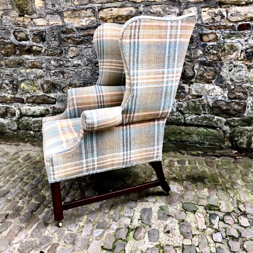 A George III mahogany wing armchair upholstered in a blue, ochre, and cream tartan wool fabric with out-scrolled arms and square legs on brass castors. View V
