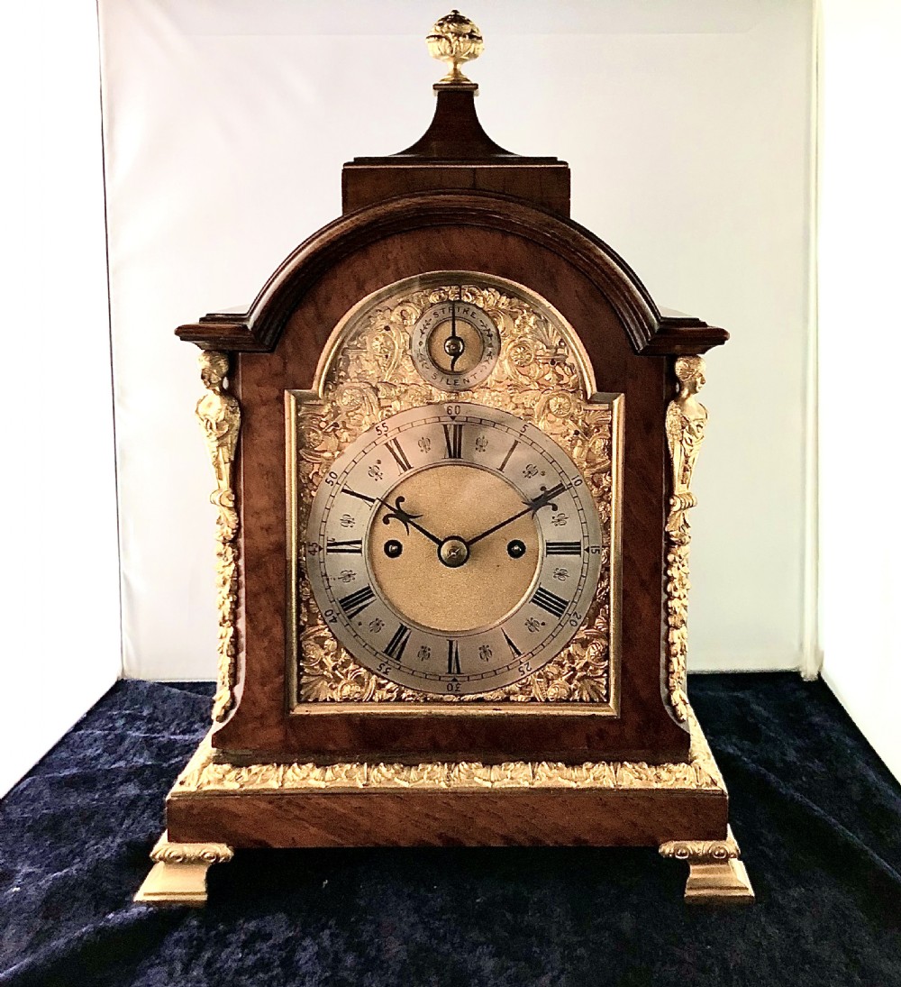 A late 19th-century mahogany bracket clock featuring an arched silvered dial, gilt-bronze caryatid mounts, and a brass finial top.