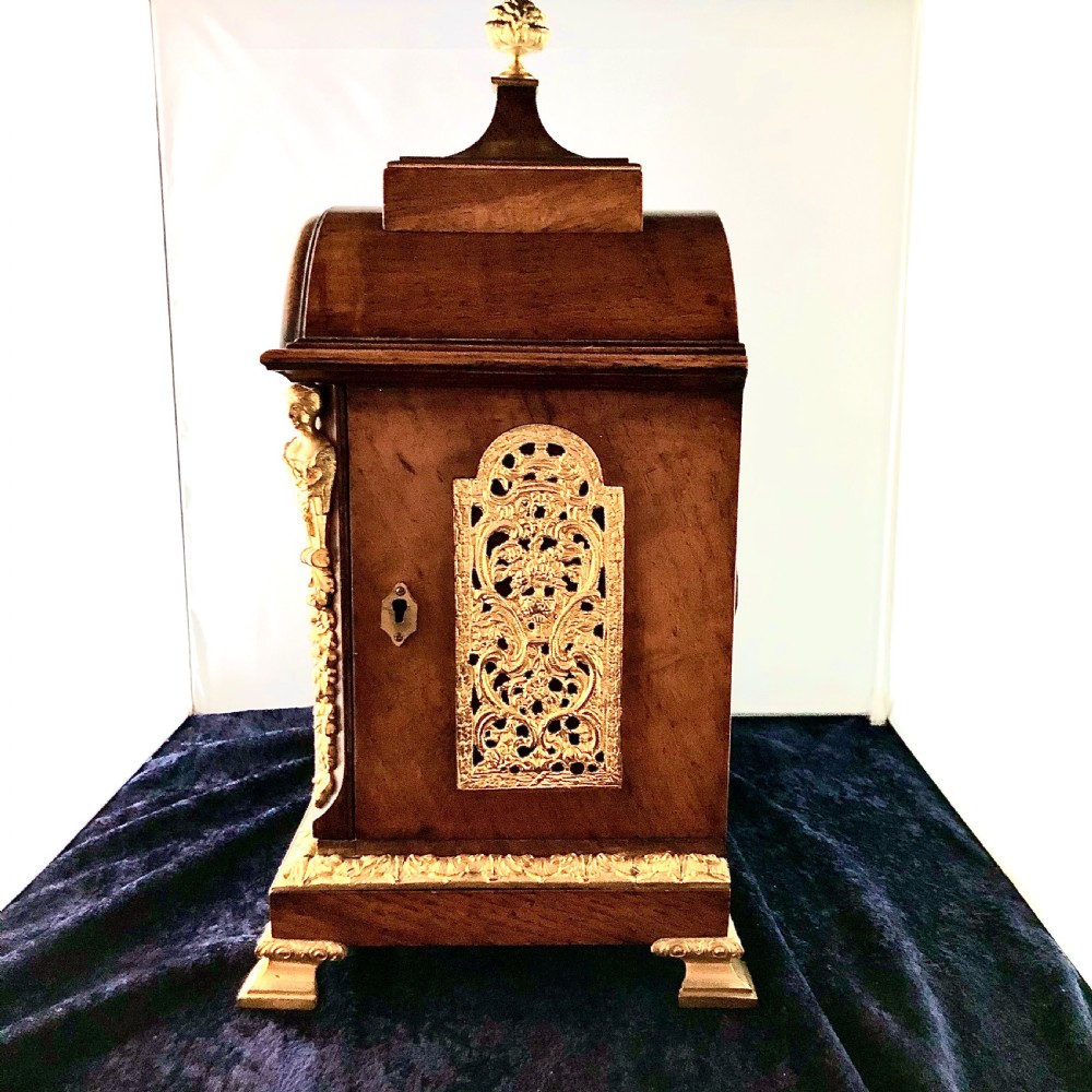 A late 19th-century mahogany bracket clock featuring an arched silvered dial, gilt-bronze caryatid mounts, and a brass finial top. View V