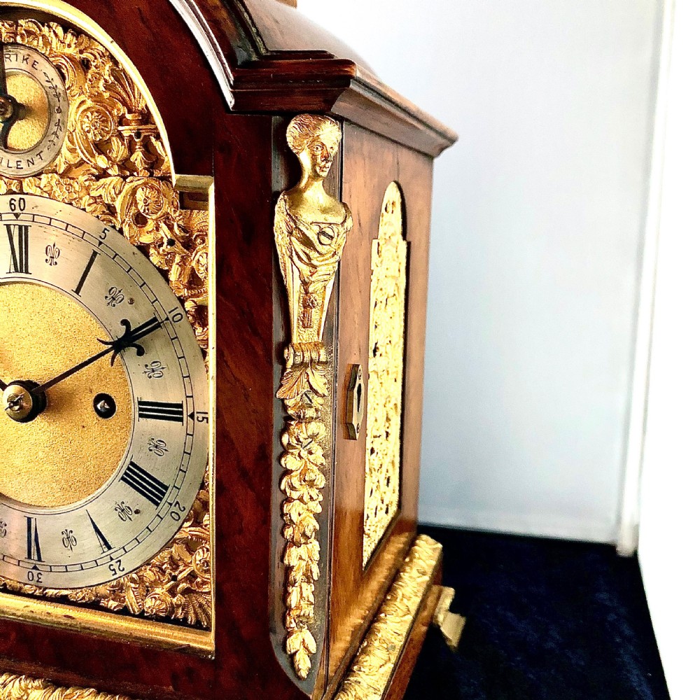 A late 19th-century mahogany bracket clock featuring an arched silvered dial, gilt-bronze caryatid mounts, and a brass finial top. View X