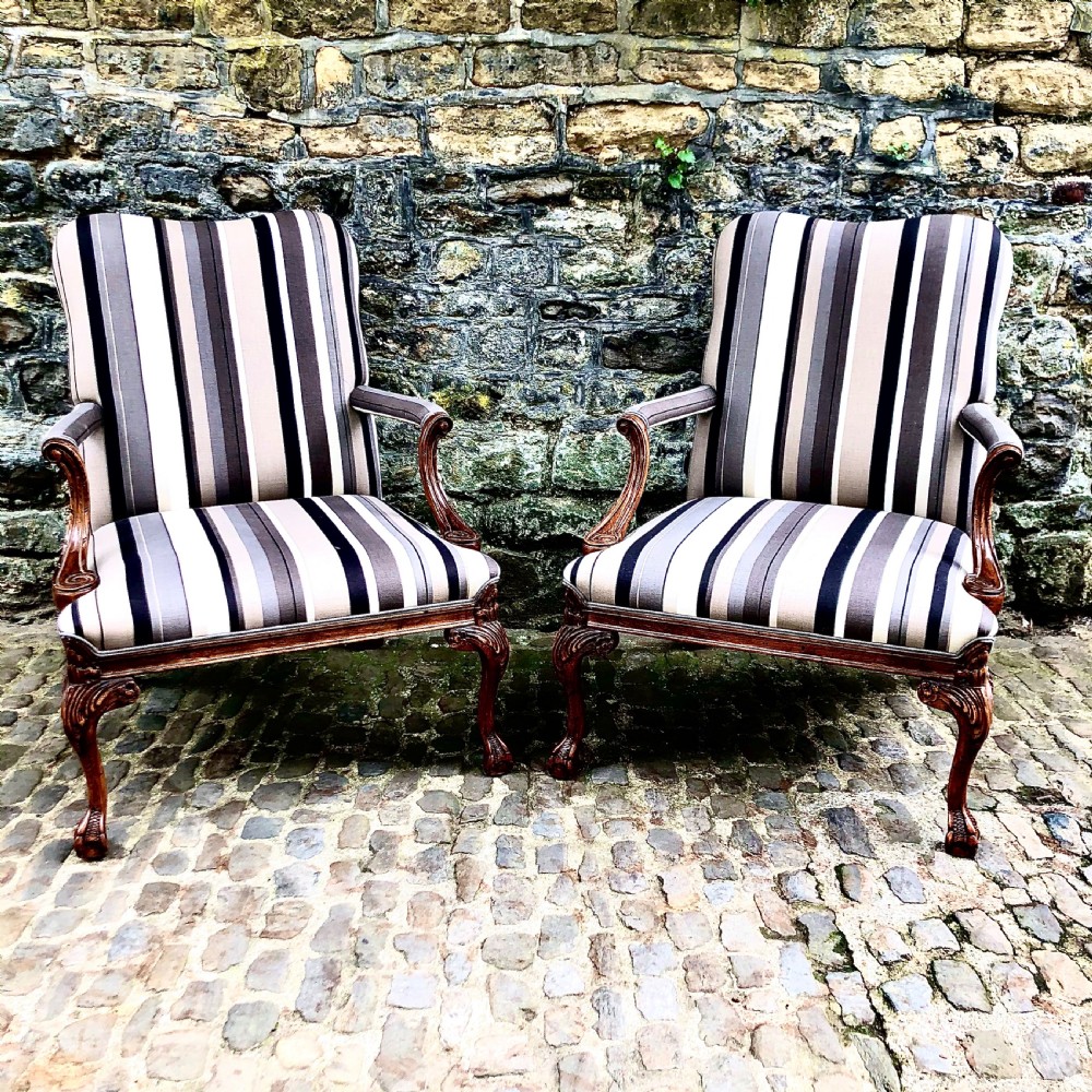 A pair of carved walnut Gainsborough armchairs upholstered in vertical striped neutral fabric featuring cabriole legs with claw and ball feet.