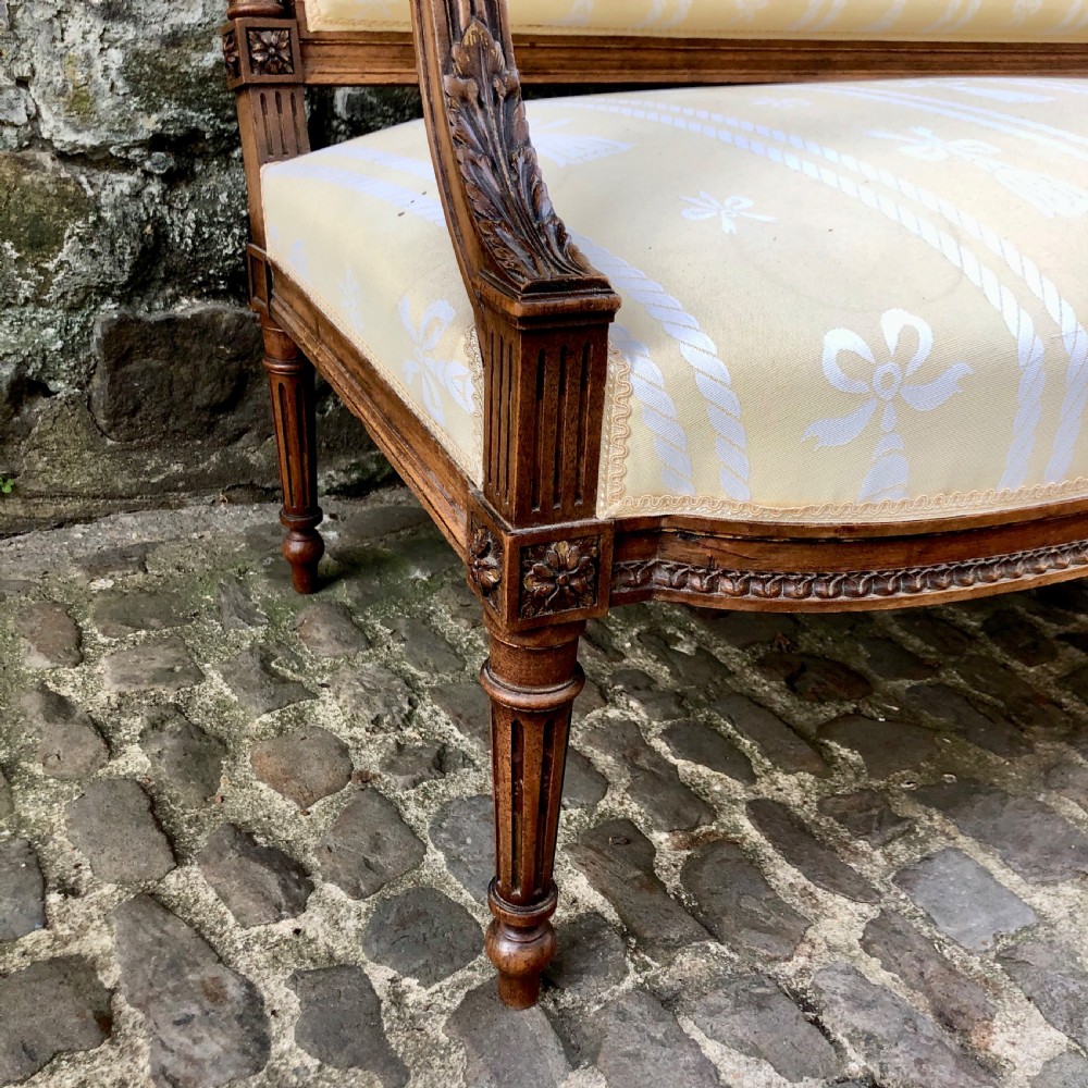 A French Second Empire carved walnut sofa featuring a cream and pale yellow striped upholstered back and seat with padded armrests and fluted legs. View VI