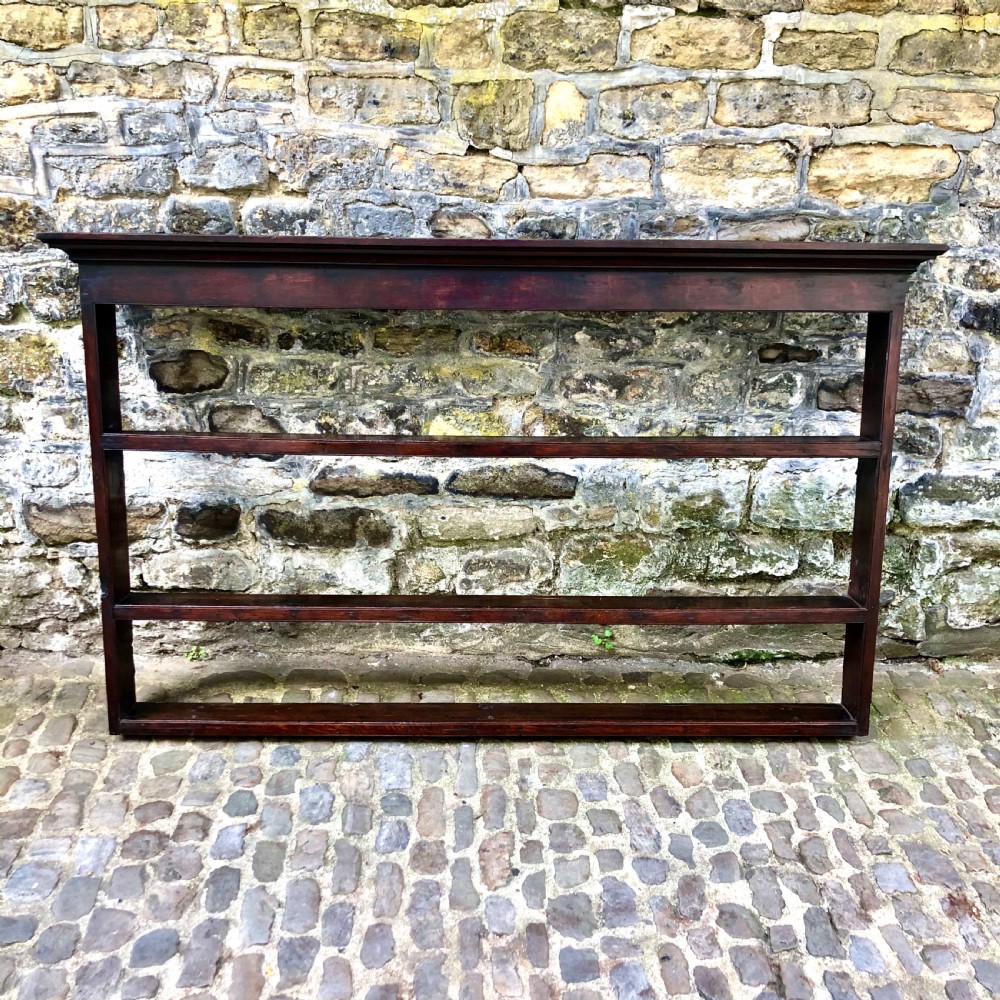 A dark oak 18th-century plate rack featuring three wide horizontal display shelves topped with a moulded cornice.