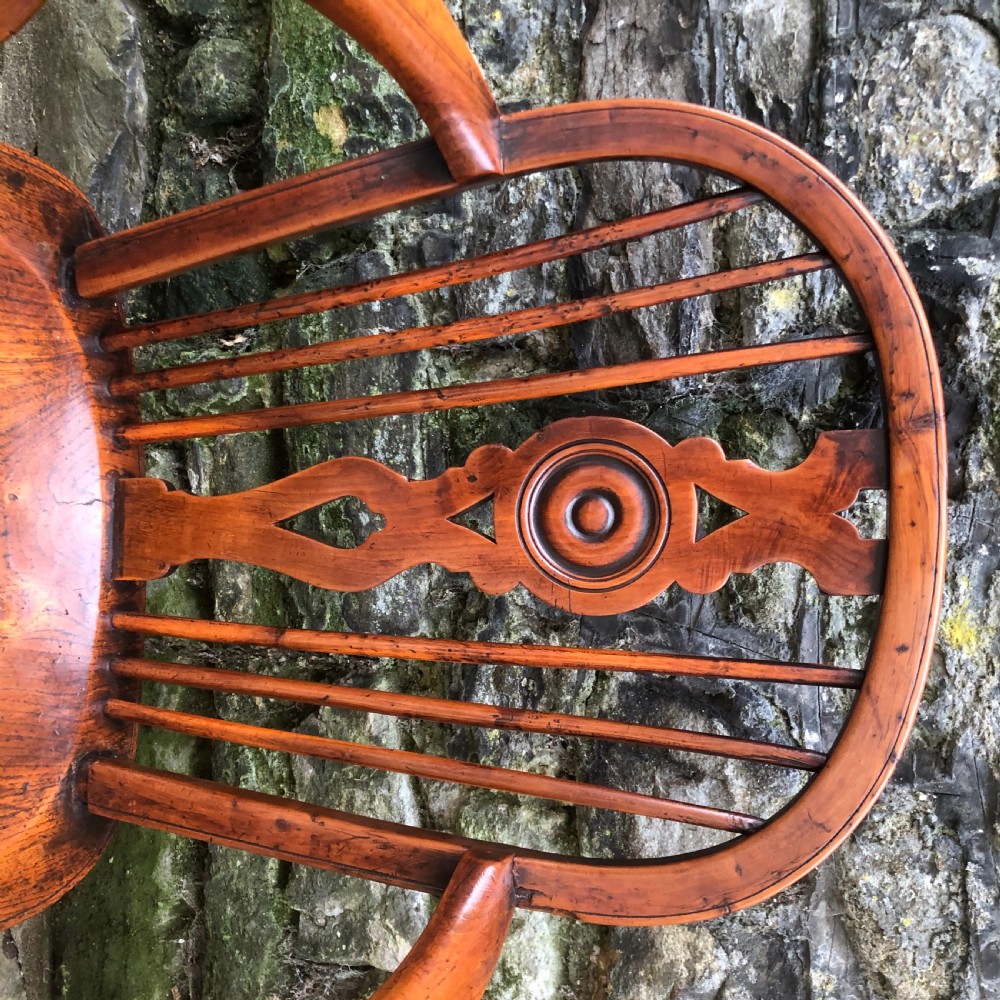 An early nineteenth-century wooden Windsor armchair featuring a shaped elm saddle seat, turned legs, curved armrests, and a pierced central splat. View V