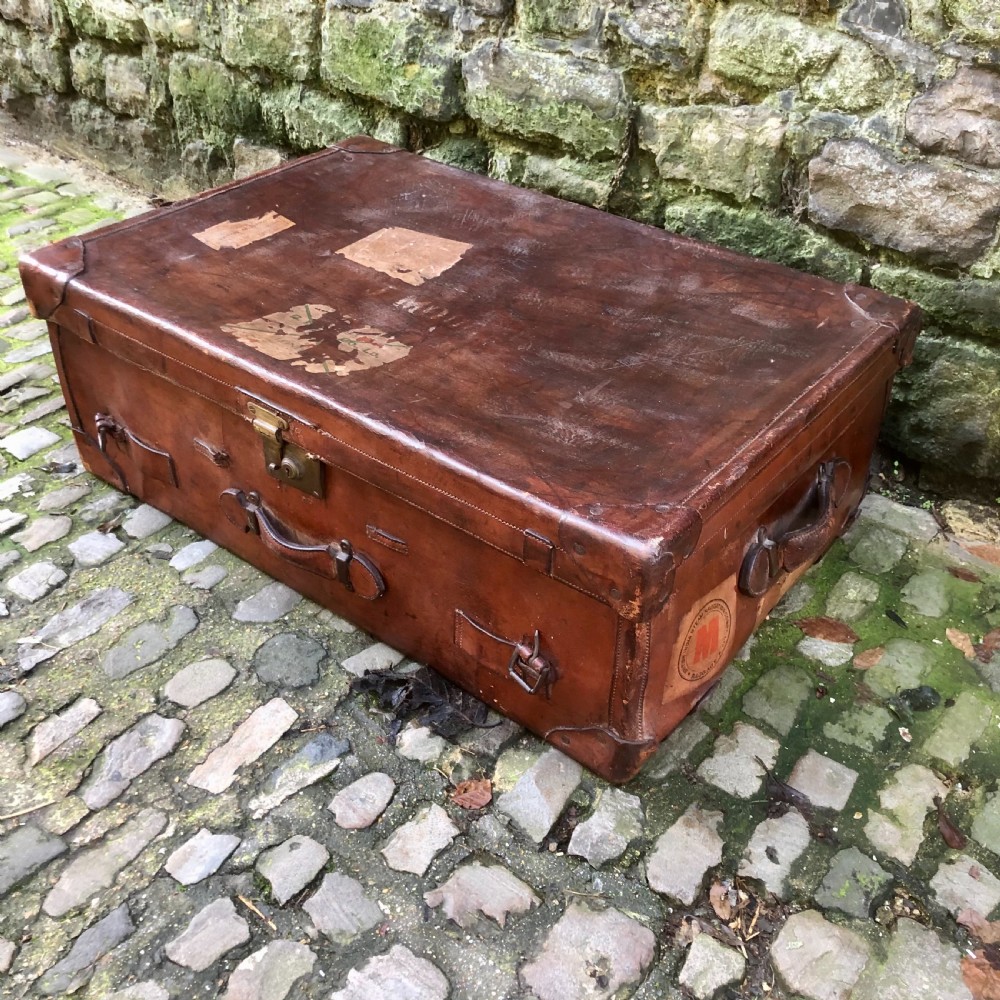 An early 20th-century warm brown leather steamer trunk with stitched corner protectors, leather straps, and a central brass lock mechanism. View II