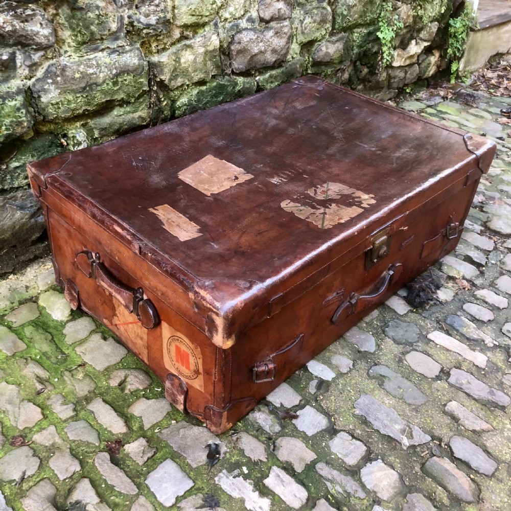 An early 20th-century warm brown leather steamer trunk with stitched corner protectors, leather straps, and a central brass lock mechanism. View III