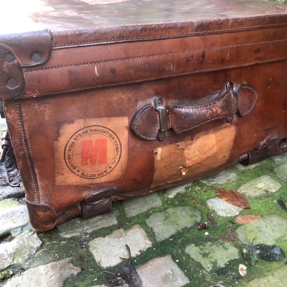An early 20th-century warm brown leather steamer trunk with stitched corner protectors, leather straps, and a central brass lock mechanism. View IV