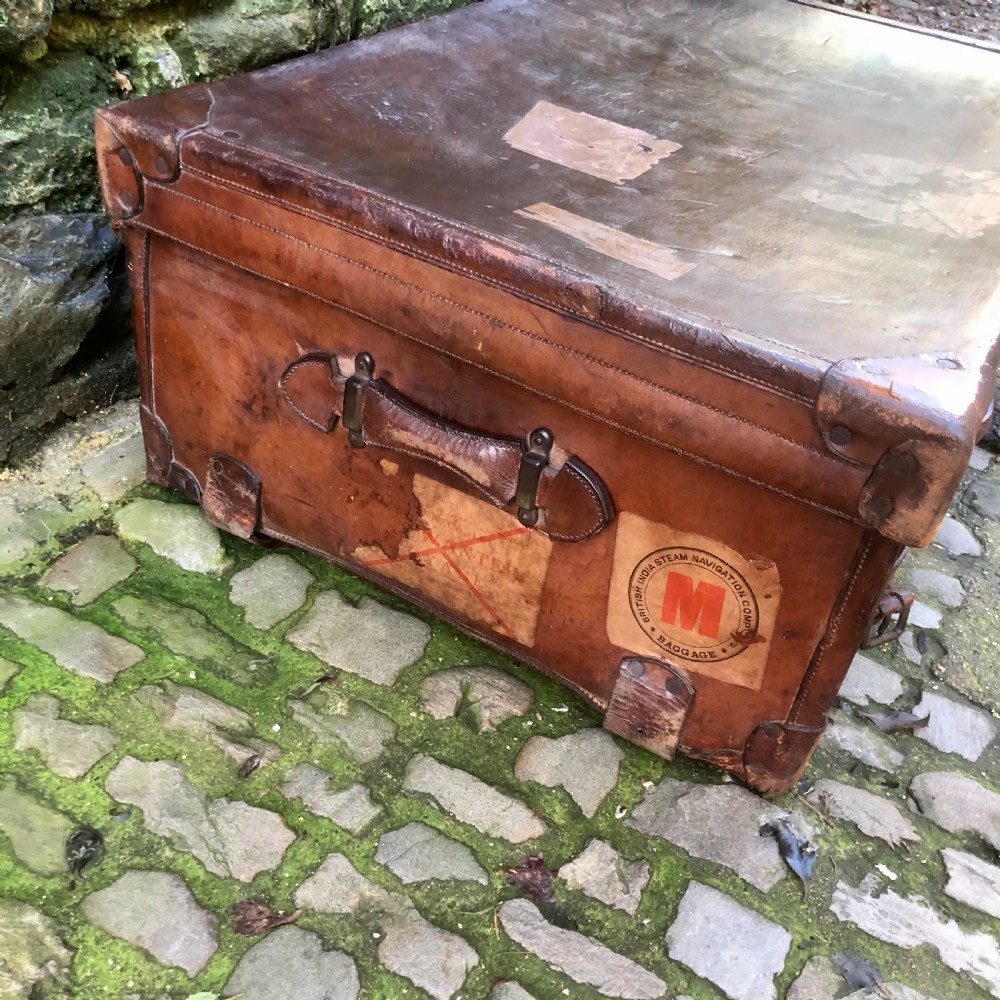 An early 20th-century warm brown leather steamer trunk with stitched corner protectors, leather straps, and a central brass lock mechanism. View VI