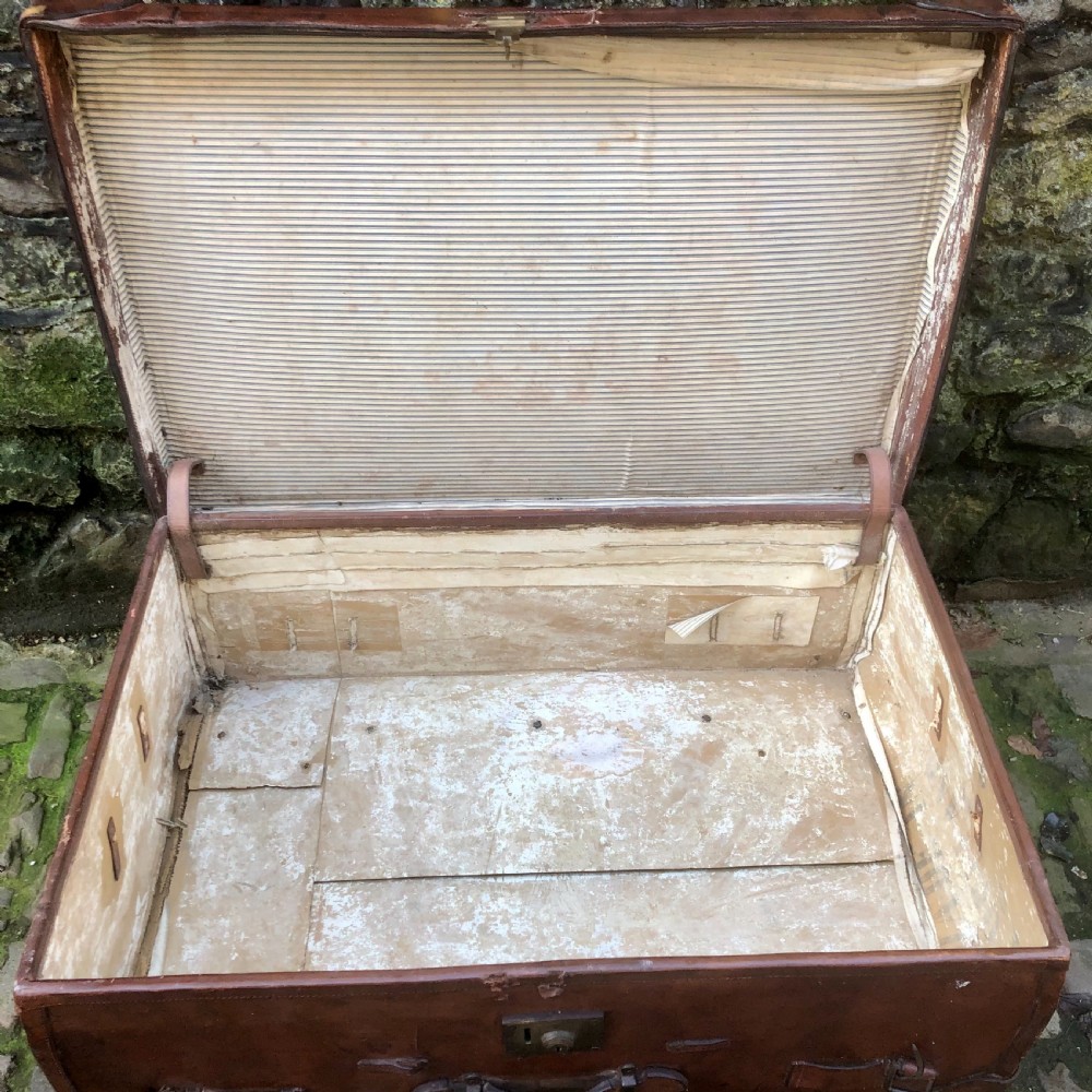 An early 20th-century warm brown leather steamer trunk with stitched corner protectors, leather straps, and a central brass lock mechanism. View VII