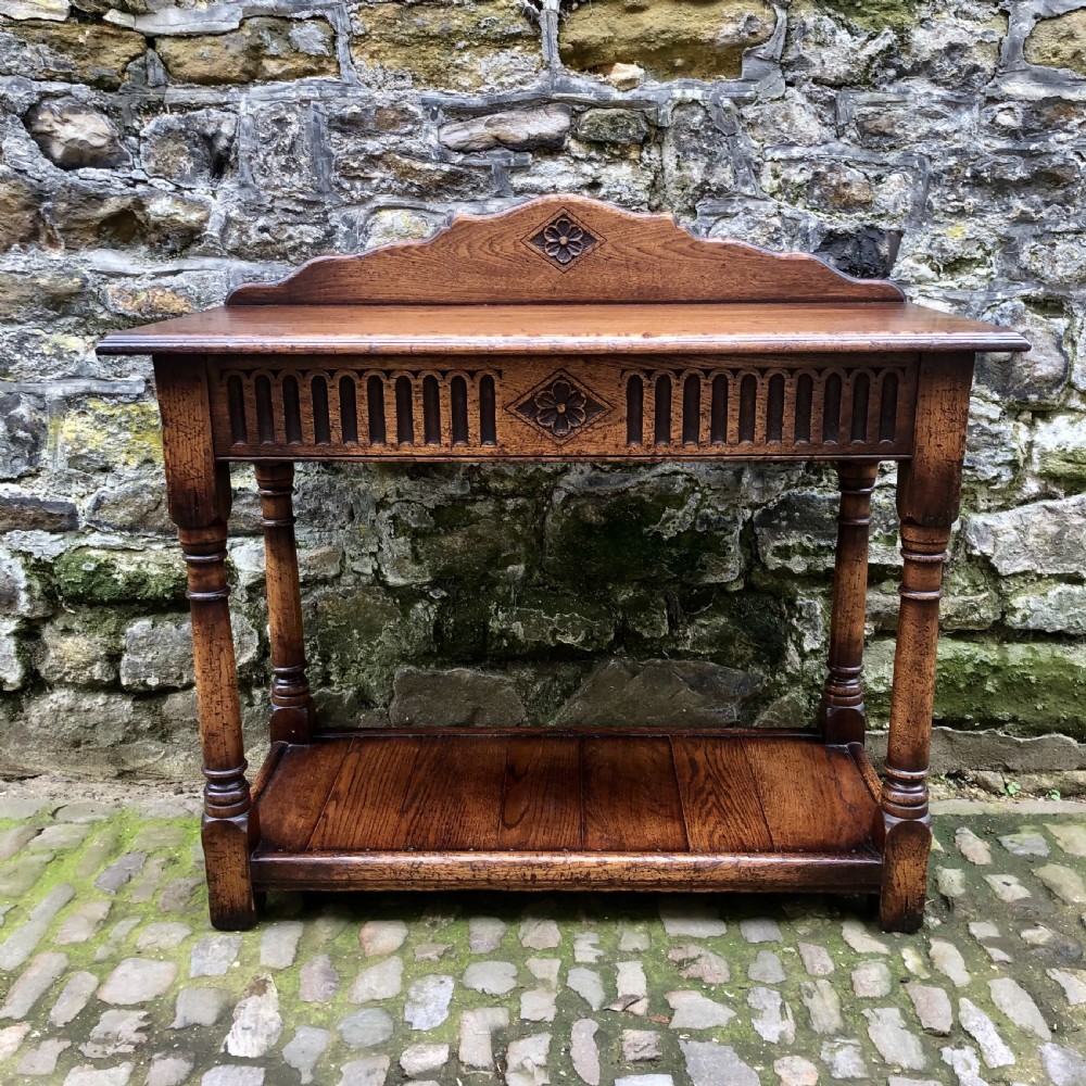 An early twentieth-century carved dark oak hall table featuring a splashback with a carved floral medallion, arcaded frieze, turned legs, and a lower shelf.