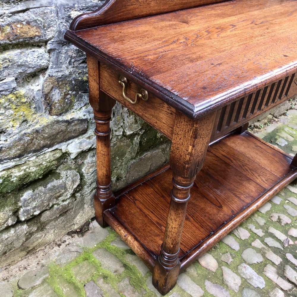 An early twentieth-century carved dark oak hall table featuring a splashback with a carved floral medallion, arcaded frieze, turned legs, and a lower shelf. View V