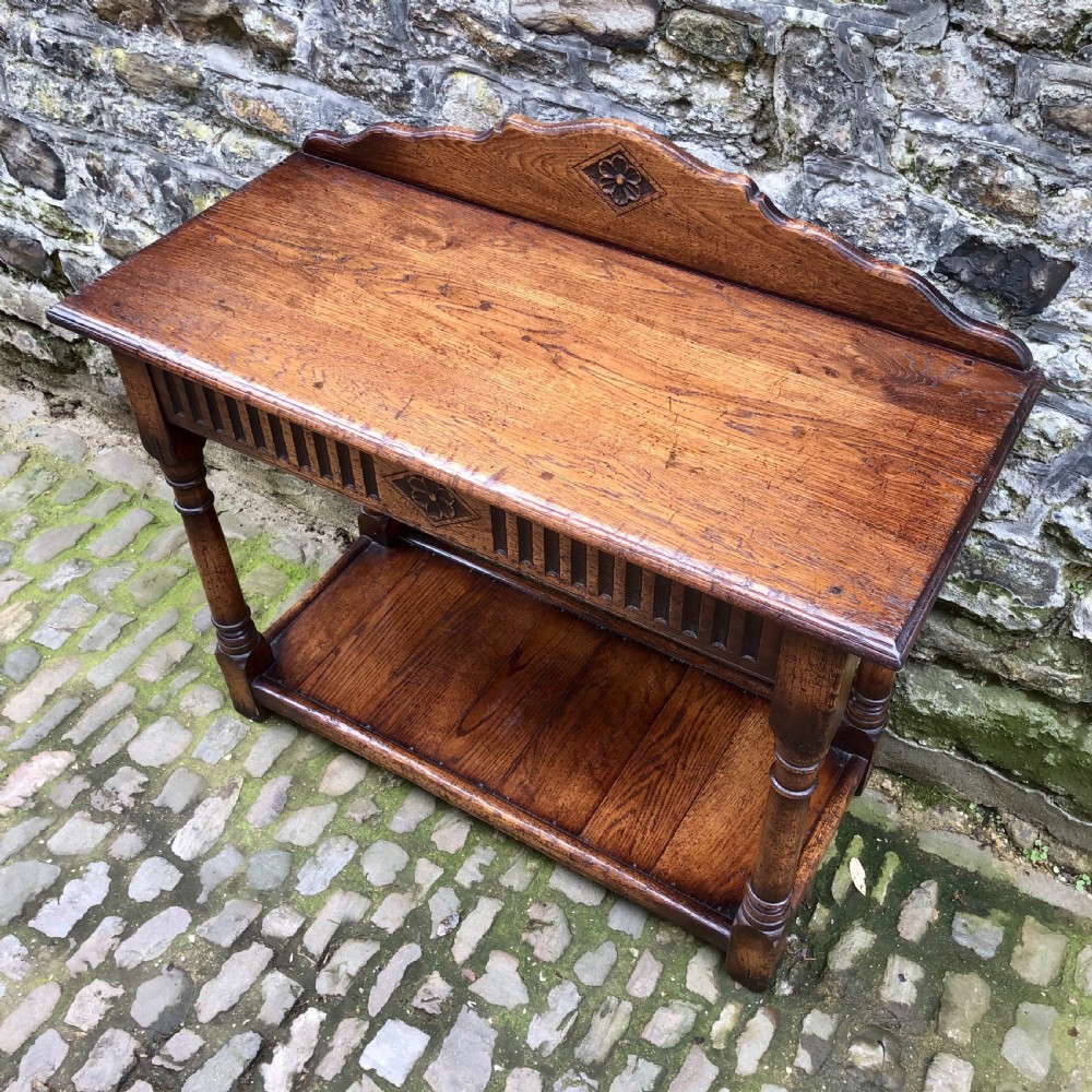 An early twentieth-century carved dark oak hall table featuring a splashback with a carved floral medallion, arcaded frieze, turned legs, and a lower shelf. View VI