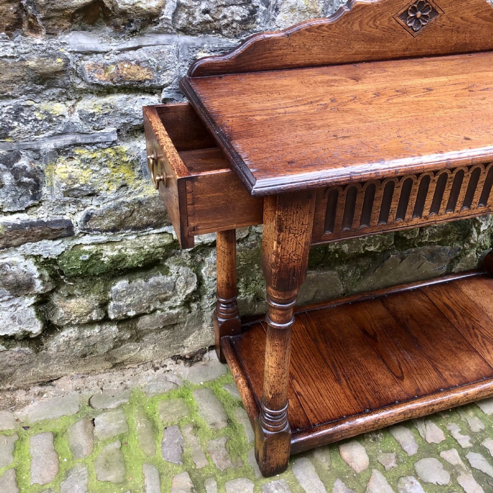An early twentieth-century carved dark oak hall table featuring a splashback with a carved floral medallion, arcaded frieze, turned legs, and a lower shelf. View VII