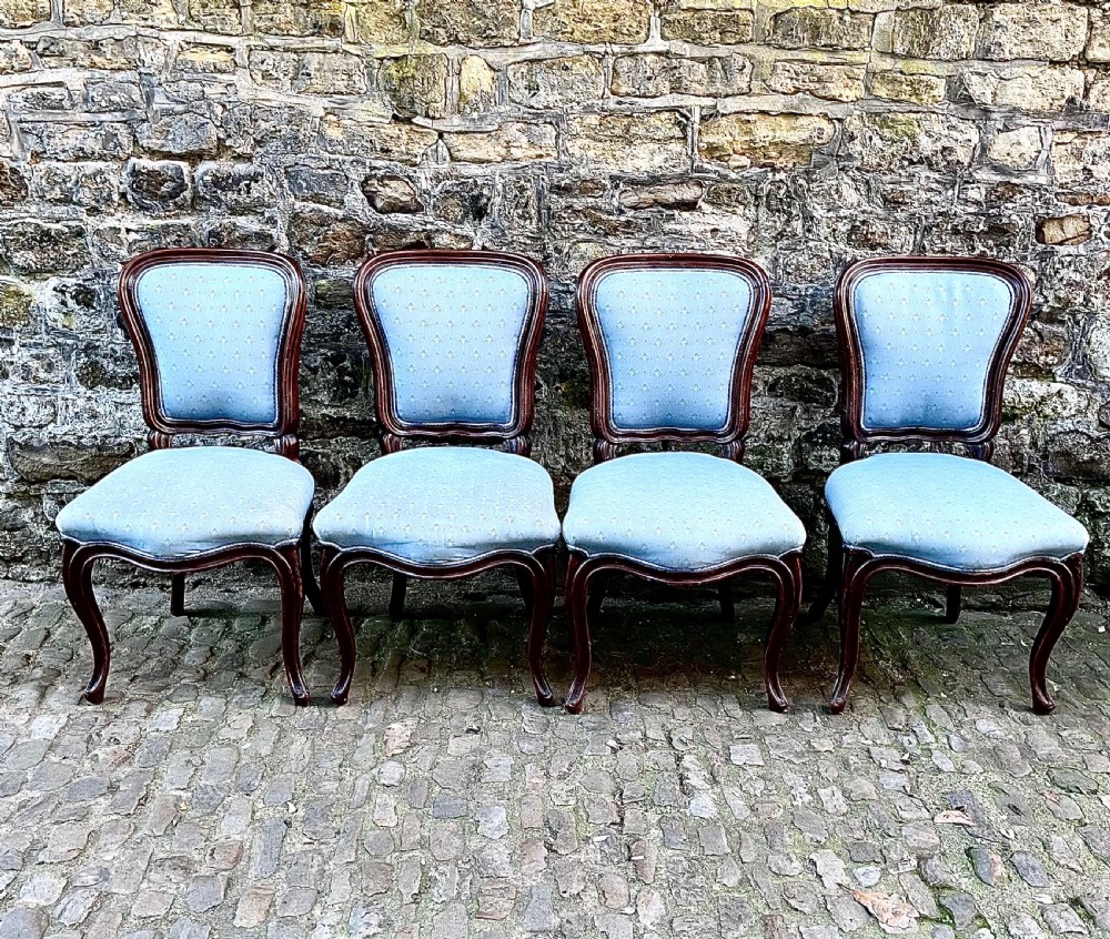 A set of four mid-19th century Louis XV style dining chairs featuring carved dark wood frames, cabriole legs, and light blue patterned fabric upholstery.