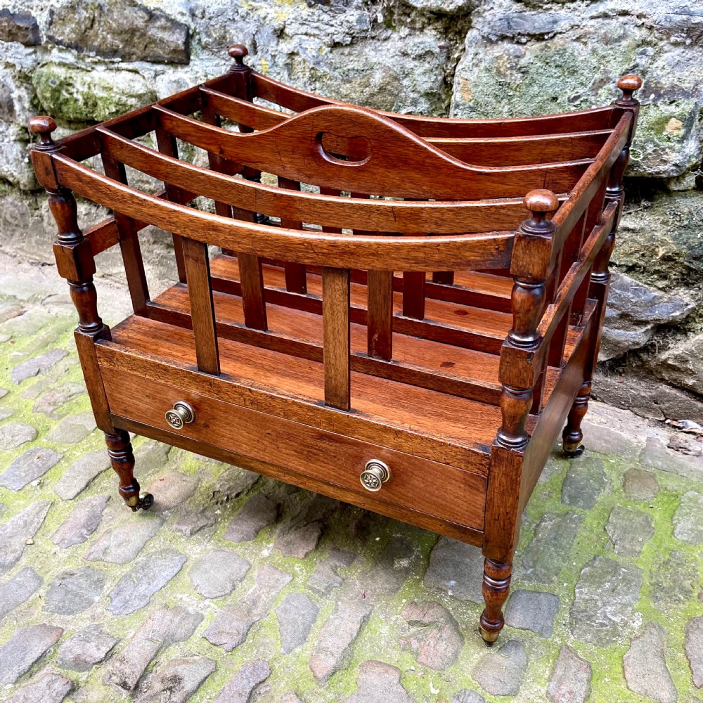 A George III mahogany Canterbury featuring four curved slatted compartments, turned corner posts topped with finials, a single base drawer with brass knobs, and turned legs on brass castors. View II