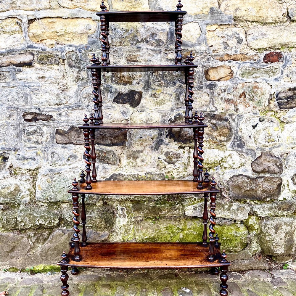 An early Victorian rosewood tiered shelf unit featuring five graduated tiers supported by turned barley twist columns and topped with finials.