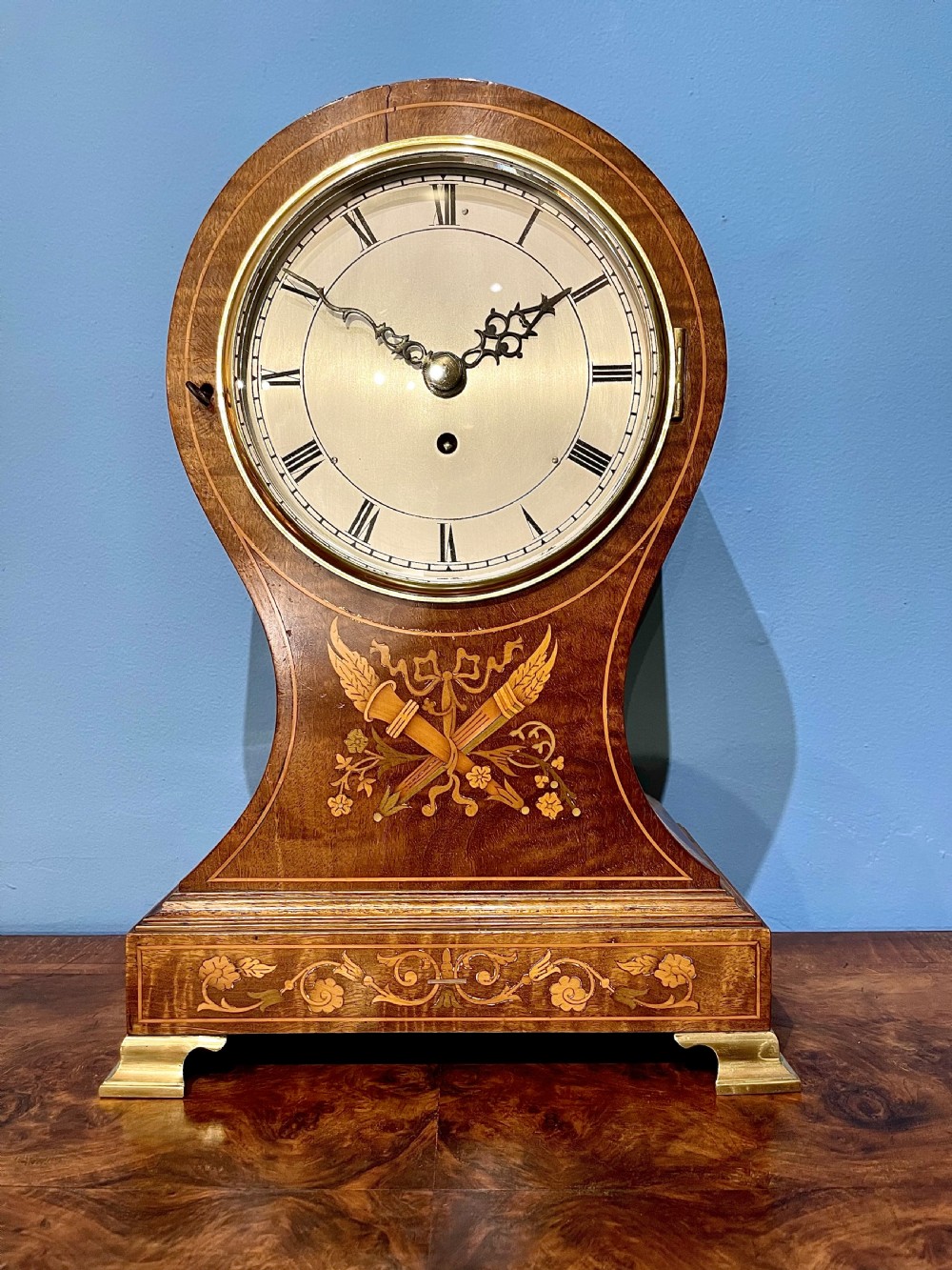A late 19th-century mahogany balloon clock featuring satinwood marquetry inlay of floral scrolls, a circular dial with Roman numerals, and brass feet.
