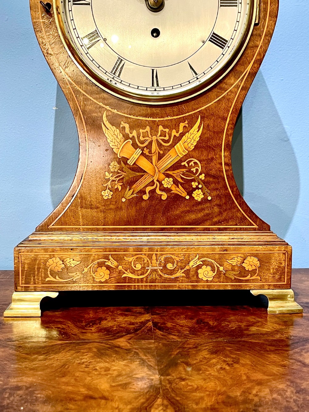 A late 19th-century mahogany balloon clock featuring satinwood marquetry inlay of floral scrolls, a circular dial with Roman numerals, and brass feet. View II