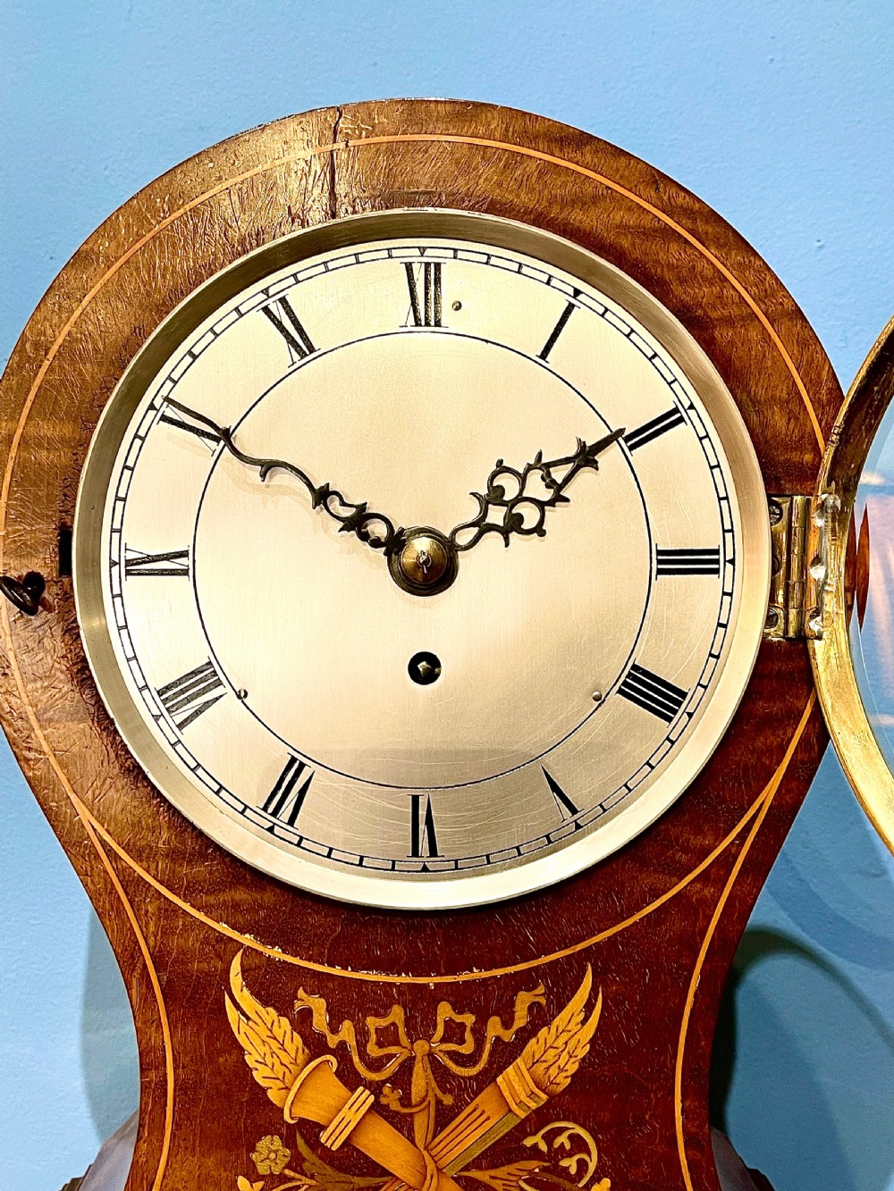 A late 19th-century mahogany balloon clock featuring satinwood marquetry inlay of floral scrolls, a circular dial with Roman numerals, and brass feet. View III