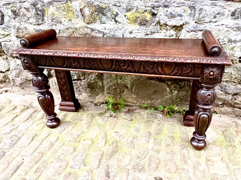 A mid-Victorian dark oak window seat featuring a carved relief frieze, turned front legs, and rolled end supports. View II