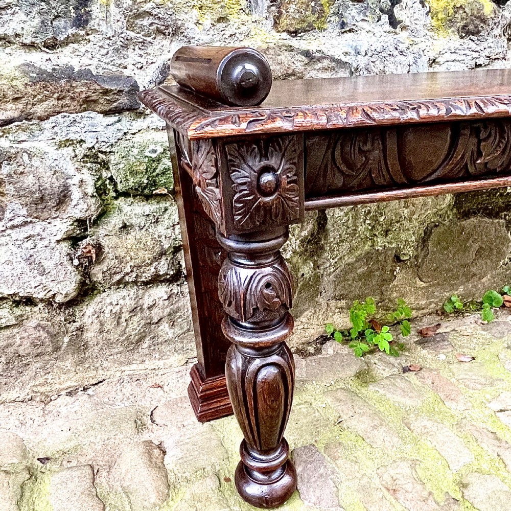 A mid-Victorian dark oak window seat featuring a carved relief frieze, turned front legs, and rolled end supports. View III