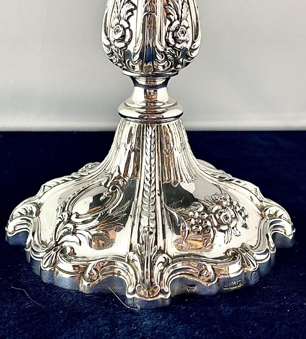 An ornate silver candlestick featuring floral repousse embossing, a contoured baluster stem, and a lobed spreading base. View II
