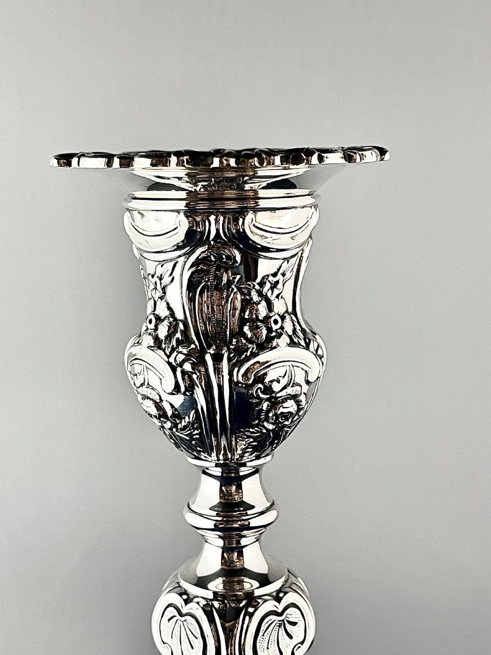 An ornate silver candlestick featuring floral repousse embossing, a contoured baluster stem, and a lobed spreading base. View III