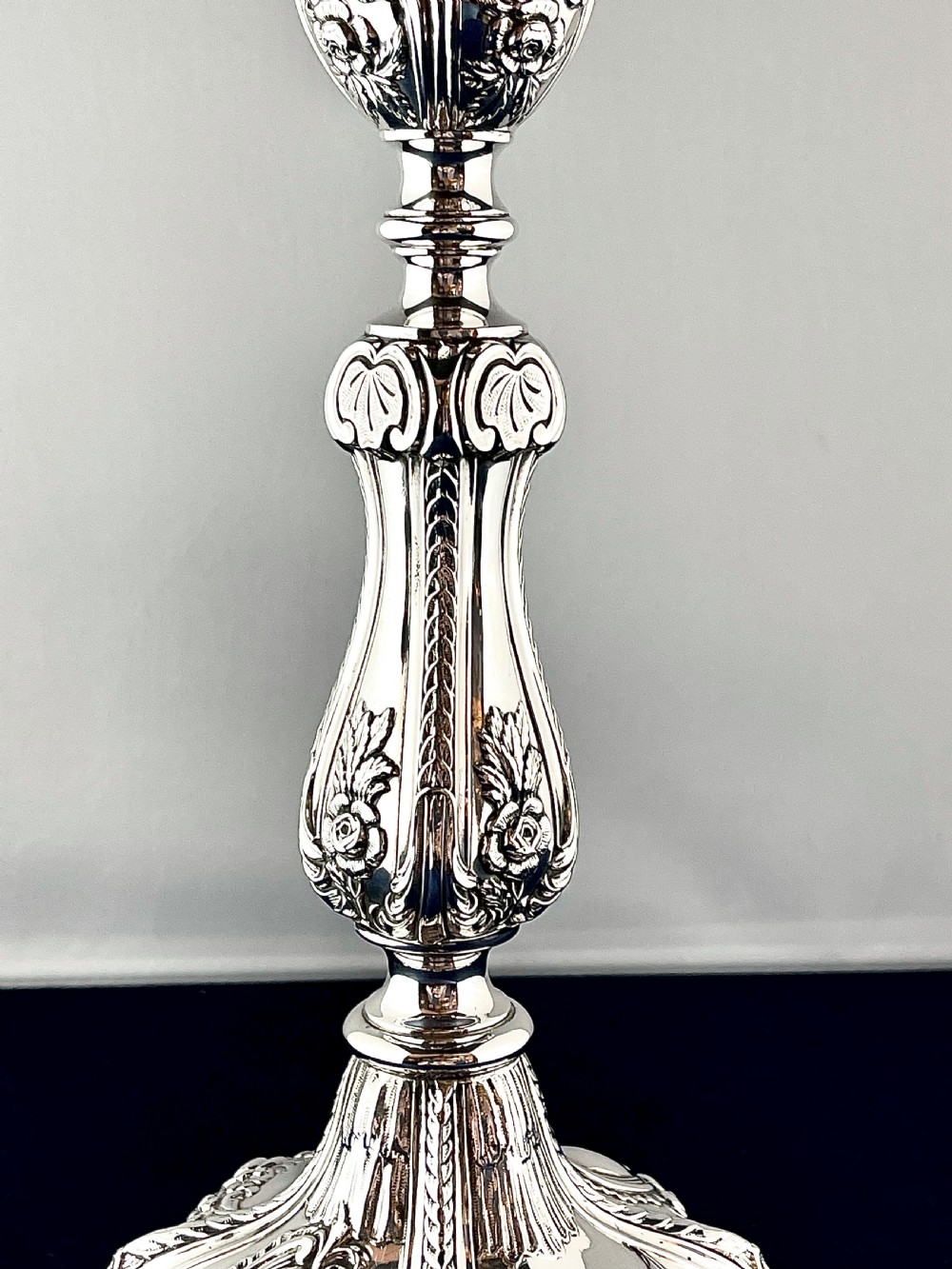 An ornate silver candlestick featuring floral repousse embossing, a contoured baluster stem, and a lobed spreading base. View IV
