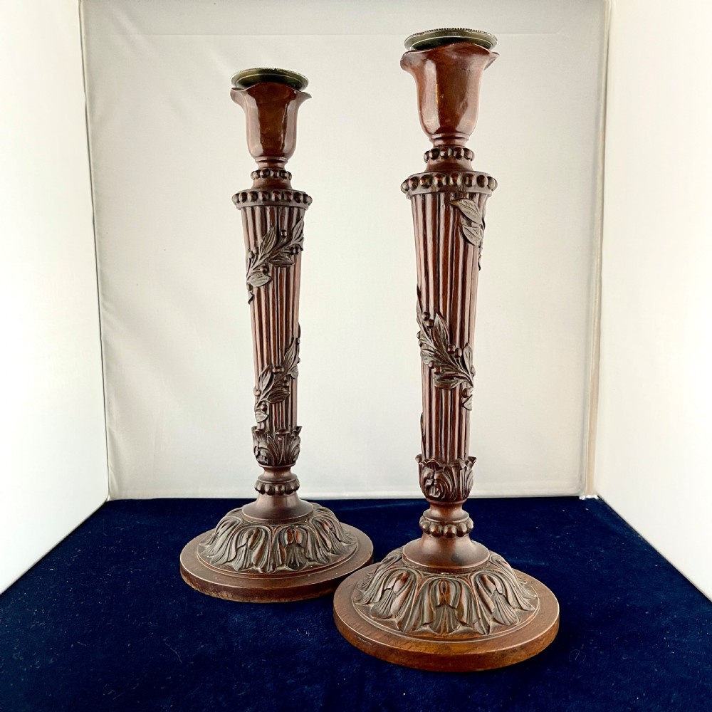 A pair of carved mahogany wooden candlesticks featuring fluted columns, leaf motifs, and circular bases in the Louis XVI style.