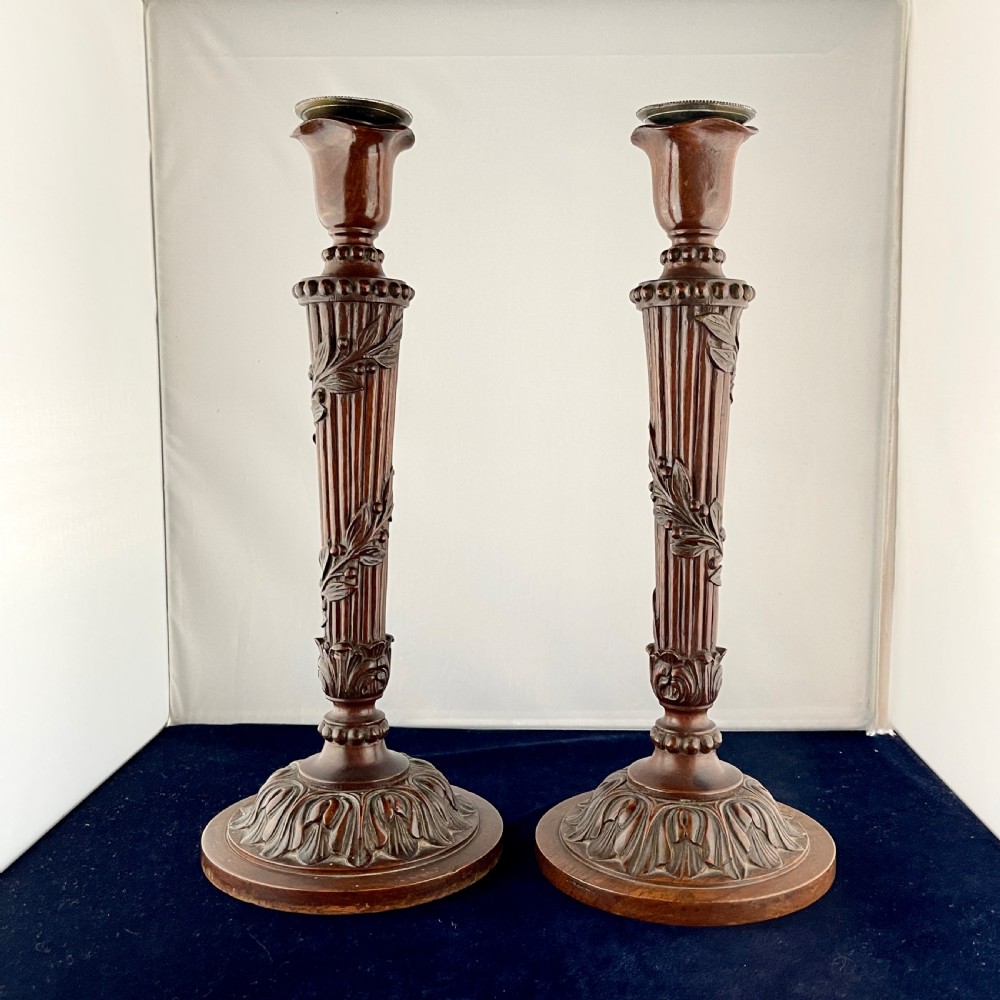 A pair of carved mahogany wooden candlesticks featuring fluted columns, leaf motifs, and circular bases in the Louis XVI style. View III