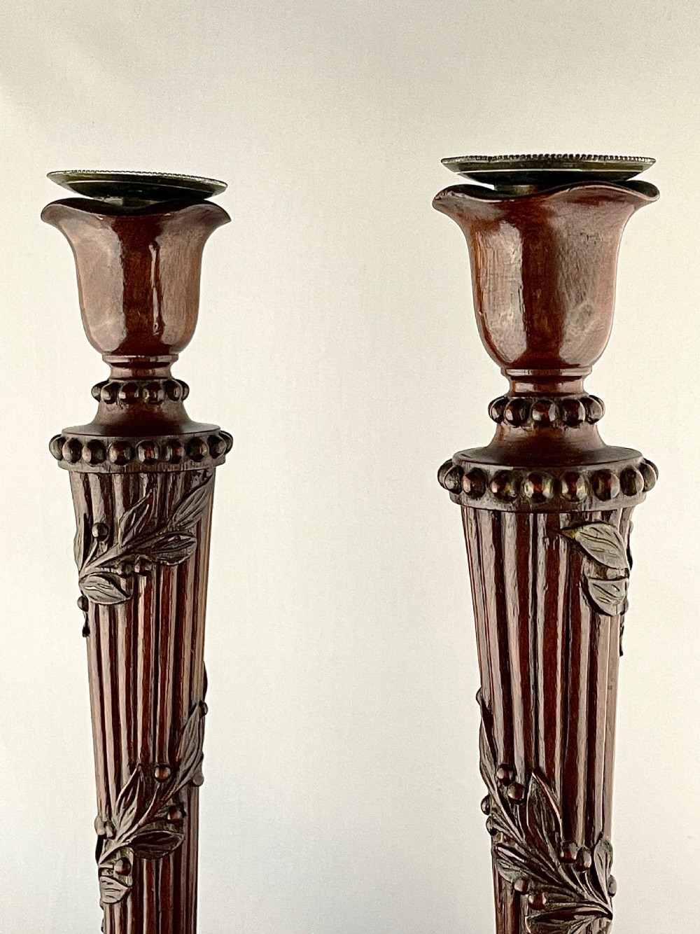 A pair of carved mahogany wooden candlesticks featuring fluted columns, leaf motifs, and circular bases in the Louis XVI style. View IV