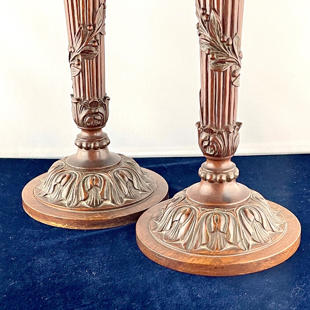 A pair of carved mahogany wooden candlesticks featuring fluted columns, leaf motifs, and circular bases in the Louis XVI style. View V