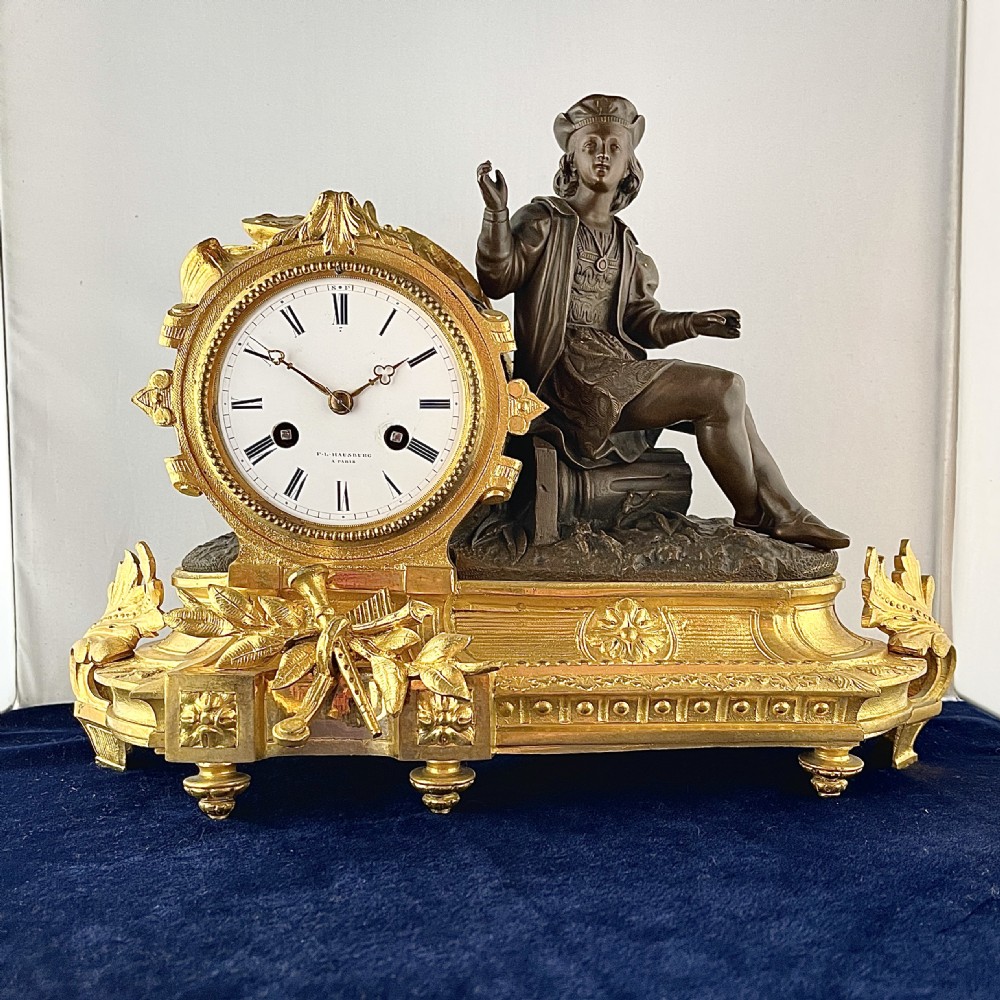A mid-19th century French mantel clock featuring a dark patinated bronze seated figure beside a gilt bronze clock drum with a white enamel dial.