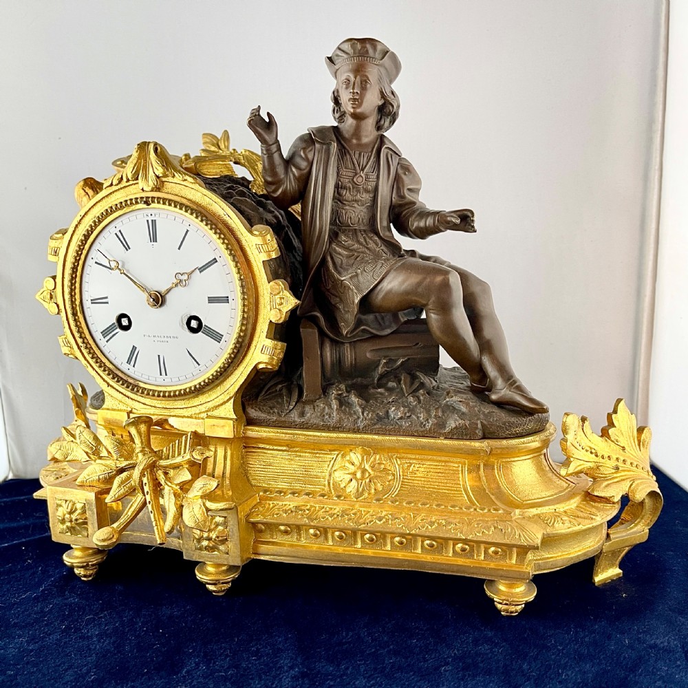 A mid-19th century French mantel clock featuring a dark patinated bronze seated figure beside a gilt bronze clock drum with a white enamel dial. View II