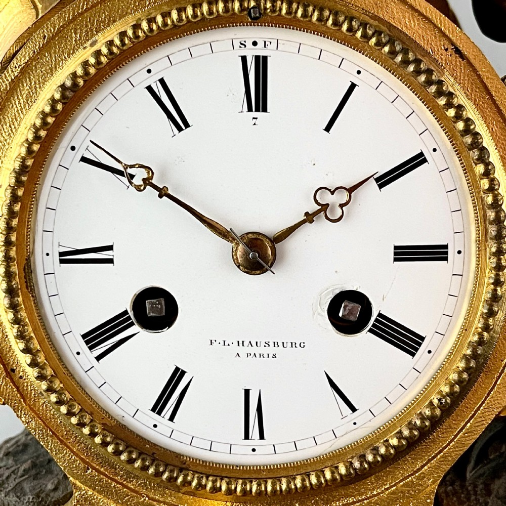 A mid-19th century French mantel clock featuring a dark patinated bronze seated figure beside a gilt bronze clock drum with a white enamel dial. View III