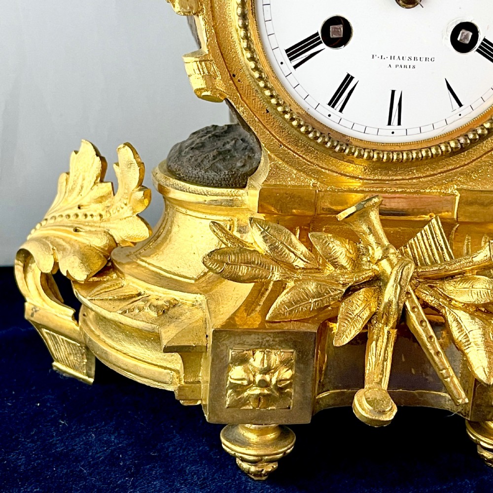 A mid-19th century French mantel clock featuring a dark patinated bronze seated figure beside a gilt bronze clock drum with a white enamel dial. View VI
