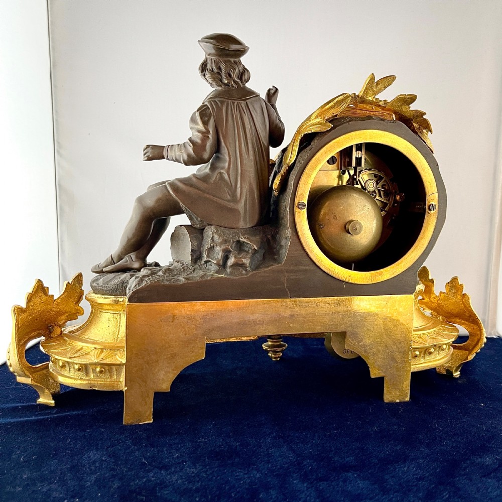 A mid-19th century French mantel clock featuring a dark patinated bronze seated figure beside a gilt bronze clock drum with a white enamel dial. View VII