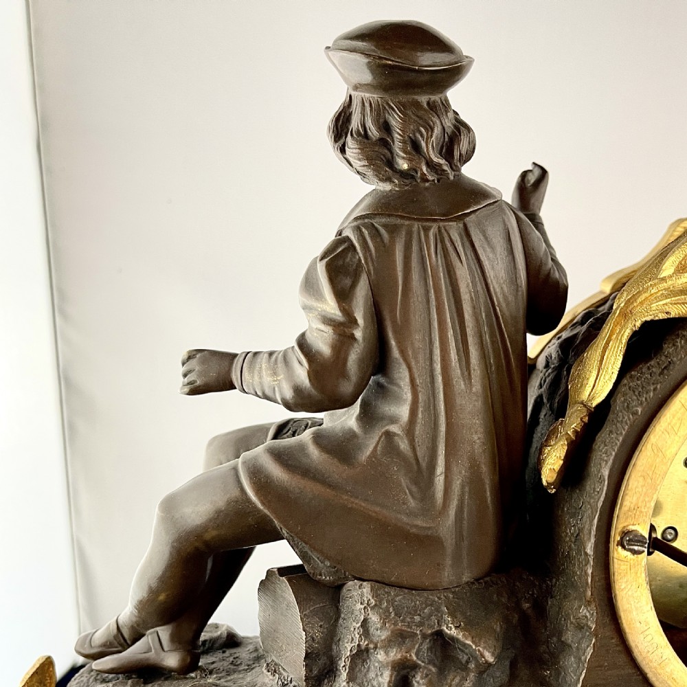 A mid-19th century French mantel clock featuring a dark patinated bronze seated figure beside a gilt bronze clock drum with a white enamel dial. View VIII