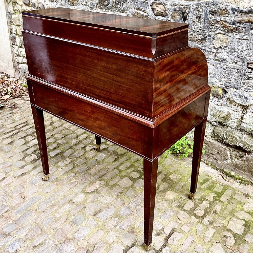 A late 19th century dark reddish-brown mahogany cylinder desk featuring a curved roll-front top, multiple drawers with brass ring handles, and tapered square legs on brass castors. View VIII