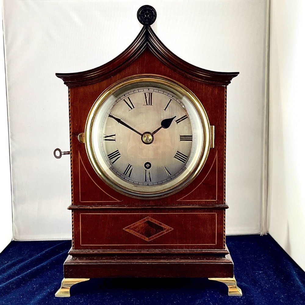 A late nineteenth-century mahogany bracket clock featuring an arched pagoda top, brass bezel with Roman numerals, geometric wood inlay, and brass feet.