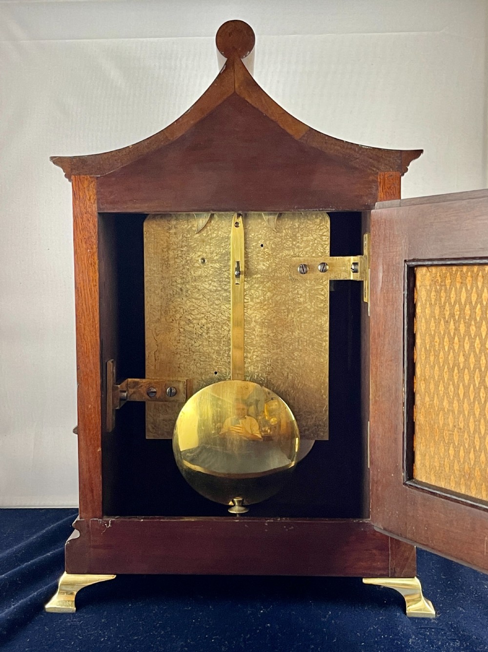 A late nineteenth-century mahogany bracket clock featuring an arched pagoda top, brass bezel with Roman numerals, geometric wood inlay, and brass feet. View II