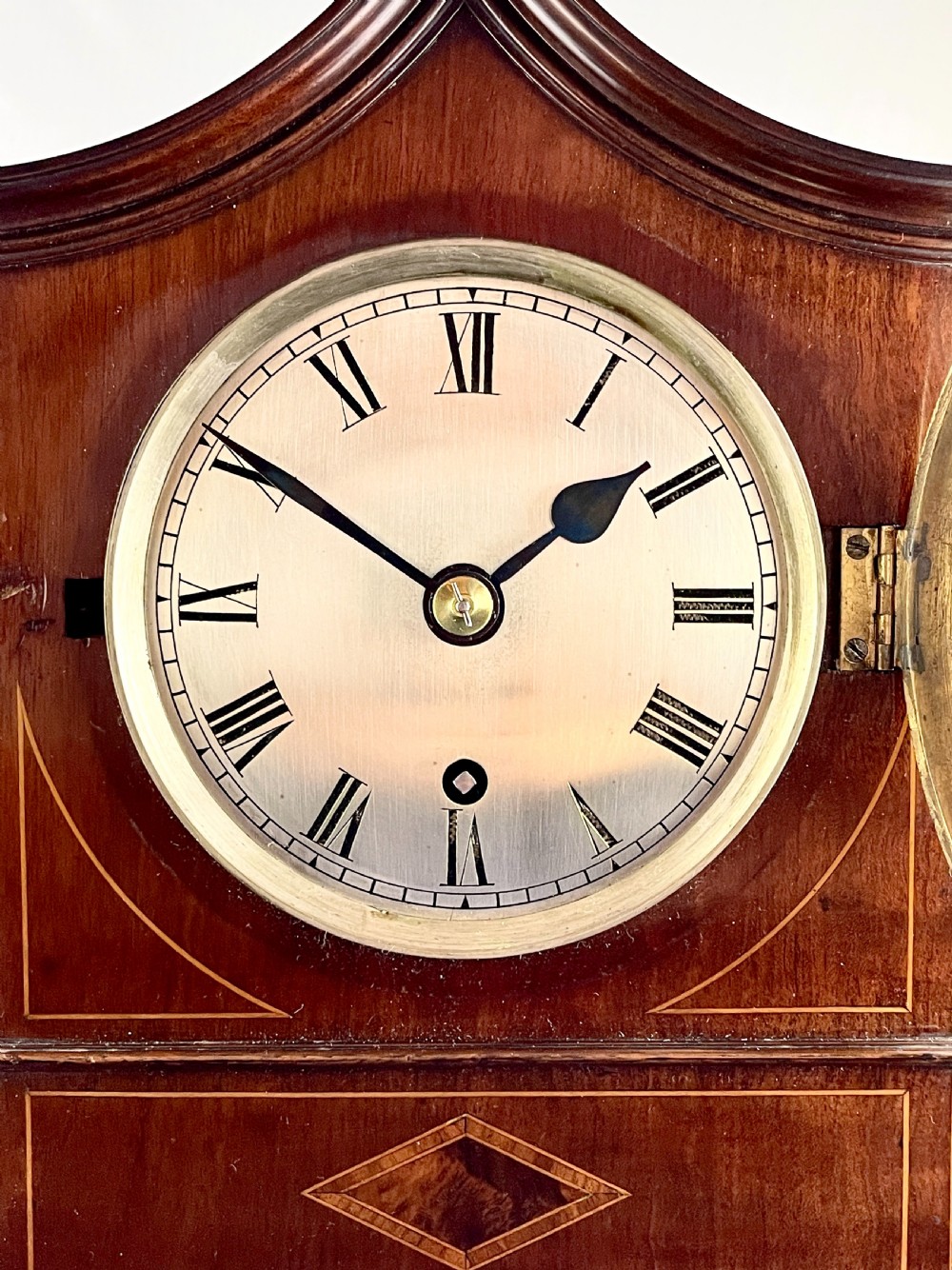 A late nineteenth-century mahogany bracket clock featuring an arched pagoda top, brass bezel with Roman numerals, geometric wood inlay, and brass feet. View III