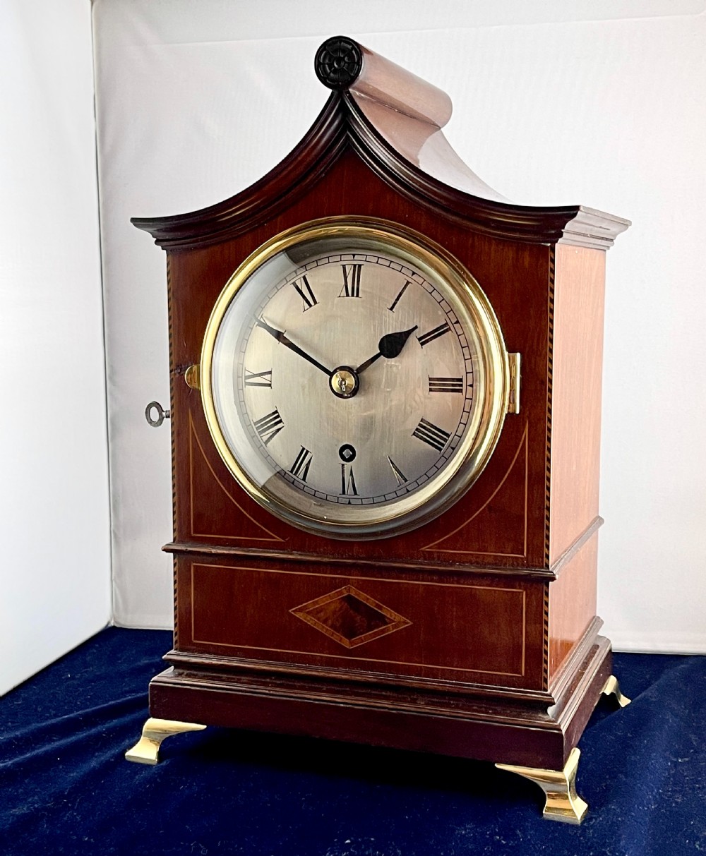 A late nineteenth-century mahogany bracket clock featuring an arched pagoda top, brass bezel with Roman numerals, geometric wood inlay, and brass feet. View IV