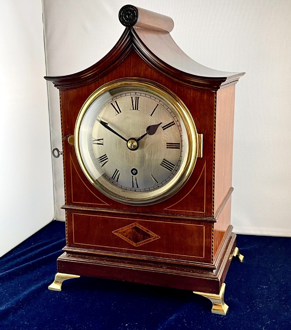 A late nineteenth-century mahogany bracket clock featuring an arched pagoda top, brass bezel with Roman numerals, geometric wood inlay, and brass feet. View V