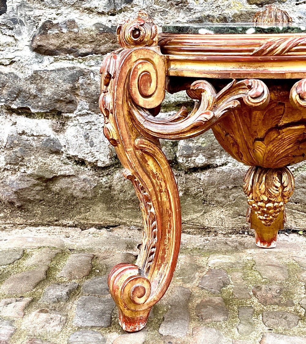 An ornate mid-19th century Italian carved giltwood pedestal stand featuring scrolling acanthus leaf legs and a circular inset green marble top. View VI