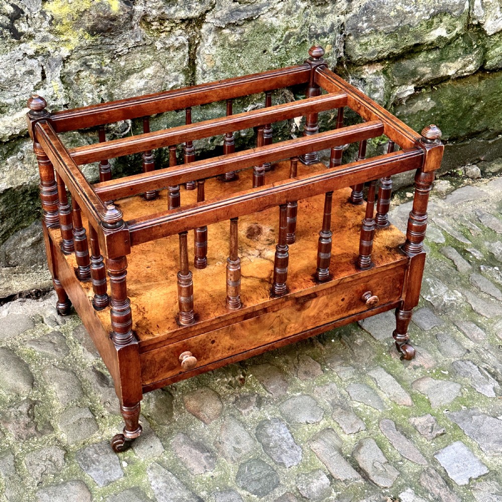 A mid-Victorian warm brown walnut Canterbury featuring turned spindles, horizontal dividers, a lower drawer with twin knobs, and turned legs on brass castors. View III