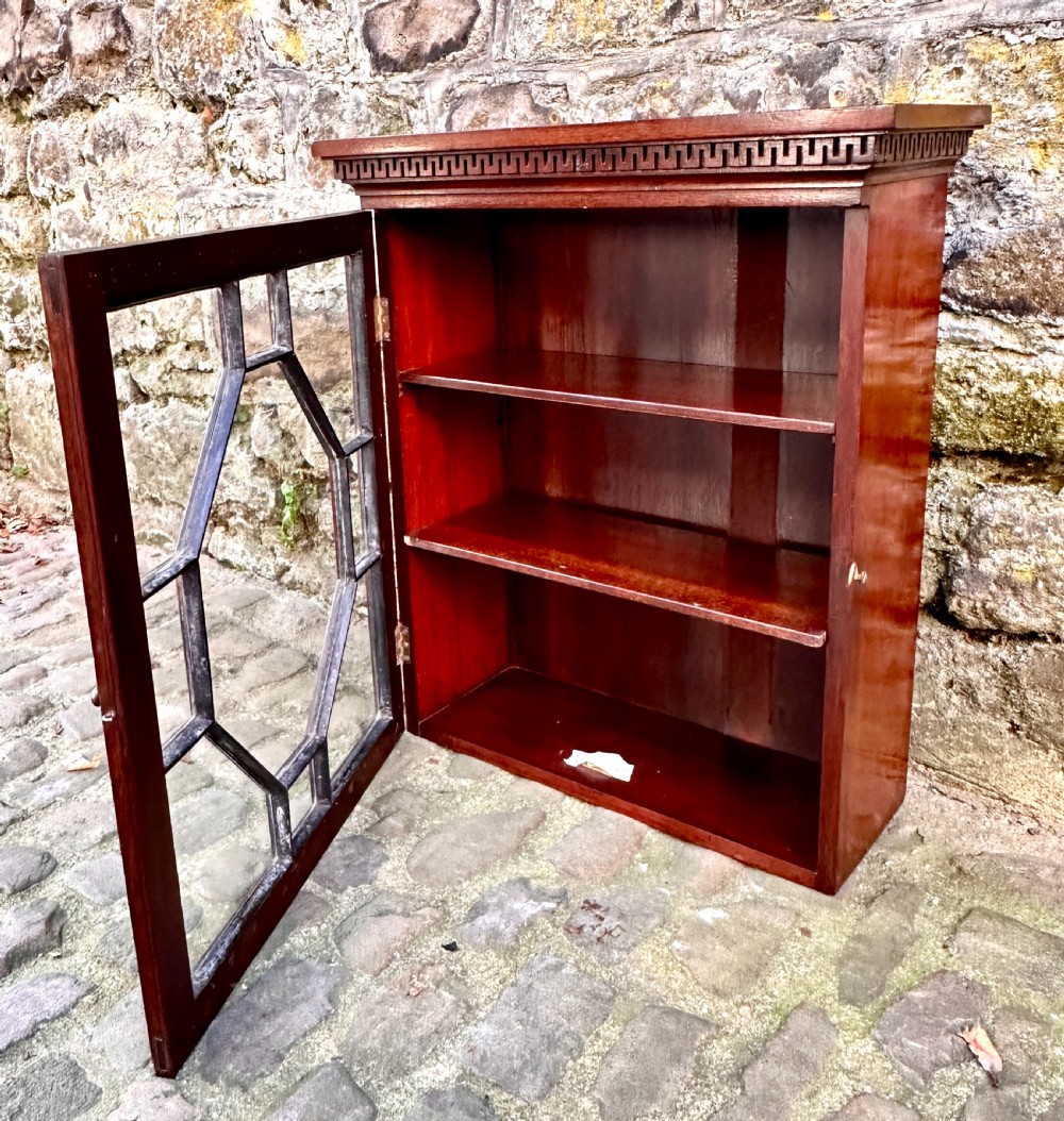 A dark mahogany Victorian wall cupboard featuring a carved Greek key frieze and a single astragal glazed door with an octagonal central glass pattern. View II